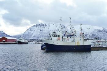 En fisketråler ligger til kais i en fjord, snødekte fly i bakgrunnen. Foto: Øivind Haug