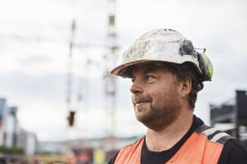 En anleggsarbeider står sidevendt mot kamera, i bakgrunnen ser vi heisekraner og hus. Foto: Øivind Haug