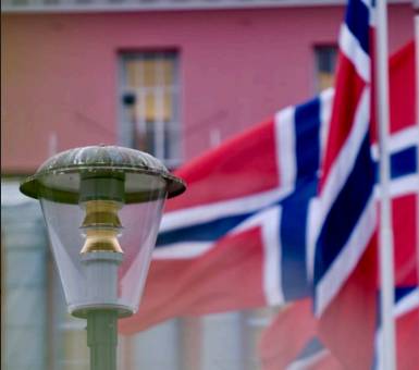 En eldre lyktestolpe foran flagg som blafrer i vinden med Rådhuset i bakgrunnen.