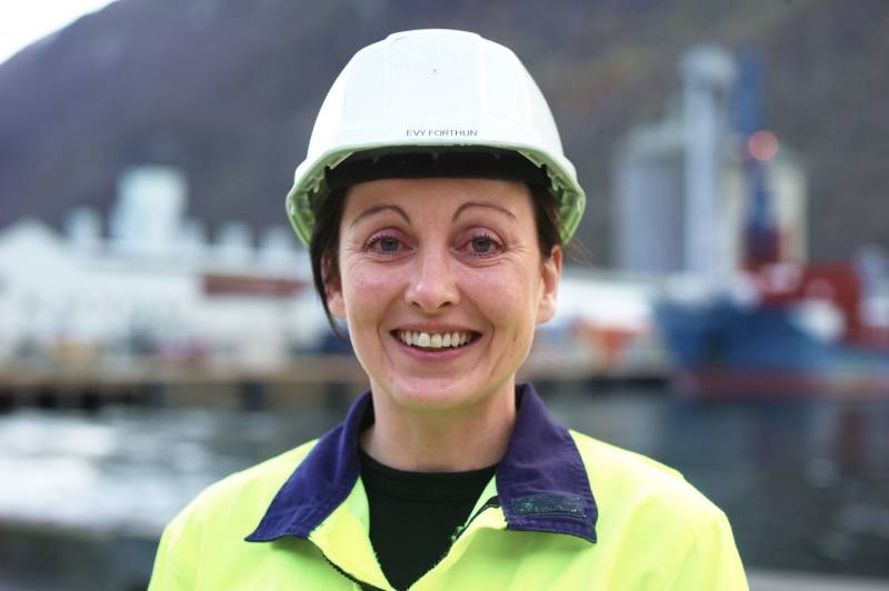En kvinnelig industriarbeider står, ikledd arbeidsklær, foran et industriområde. Foto: Øivind Haug