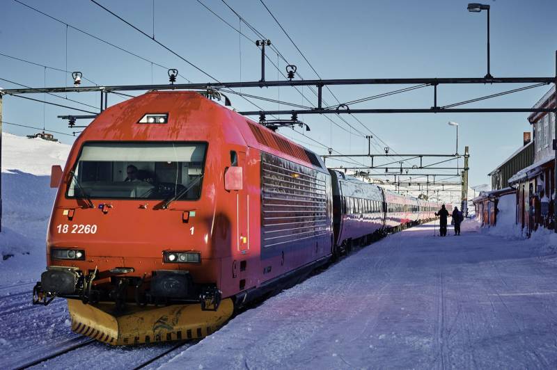 Et tog fra NSB har stoppet på en stasjon på fjellet, blå himmel og snøkledd landskap. Foto: Øivind Haug