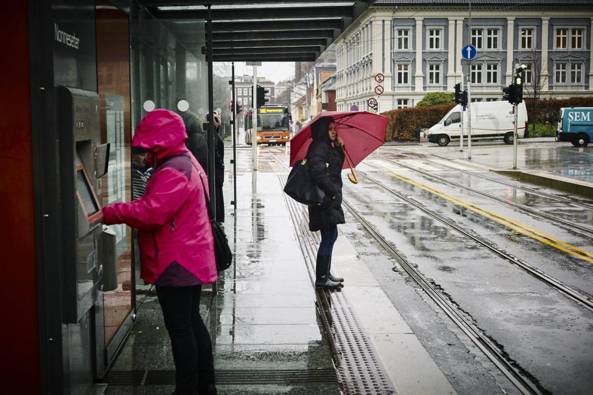 Noen mennesker står i ly av regnet og venter på bussen. Foto: Øivind Haug