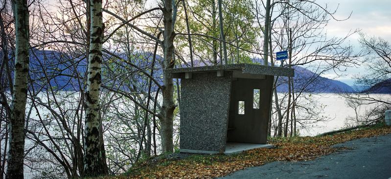 Betong buss skur stående langs veien med hav og fjell i bakgrunnen. 