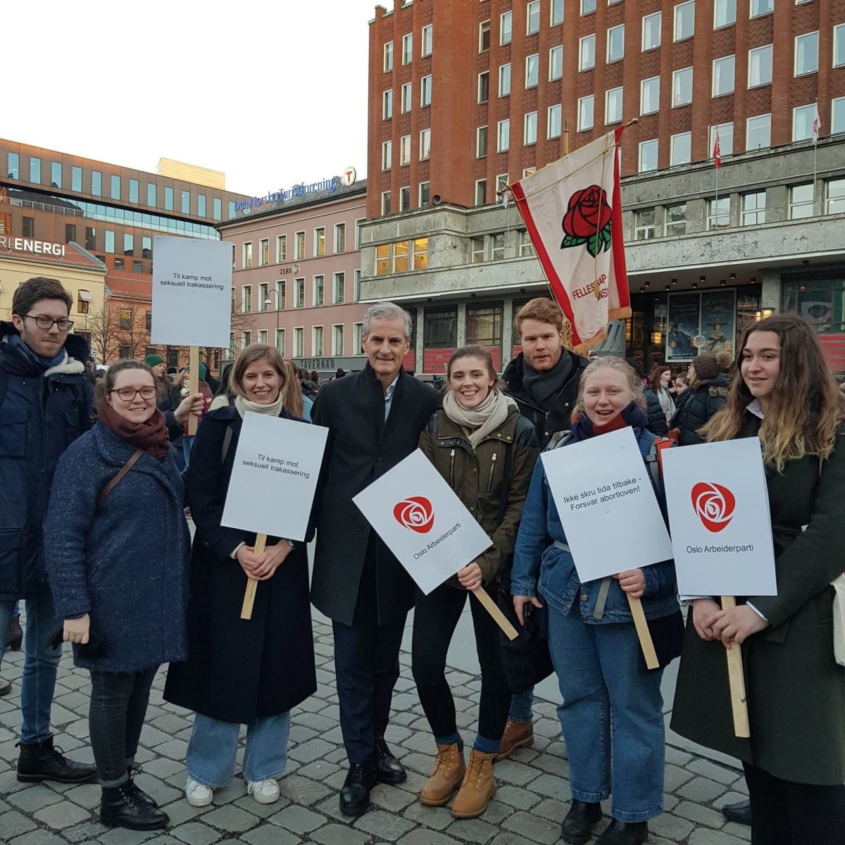 Blide medlemmer av Astud Oslo står sammen med Jonas Gahr Støre med ytterklær og plakater i forbindelse med demonstrasjon på Yopungstorget mot innskrenking av abortrettighetene for norske kvinner. Det er bilde av partikontoret og en fane for Arbeiderpartiet i bakgrunnen.