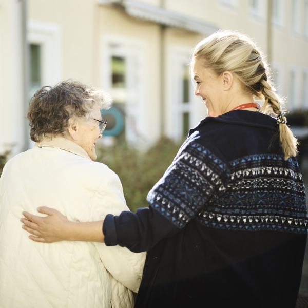 Helsearbeider og eldre dame smiler mot hverandre.