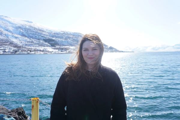 Cecilie står utendørs foran hav og fjell med vind i håret