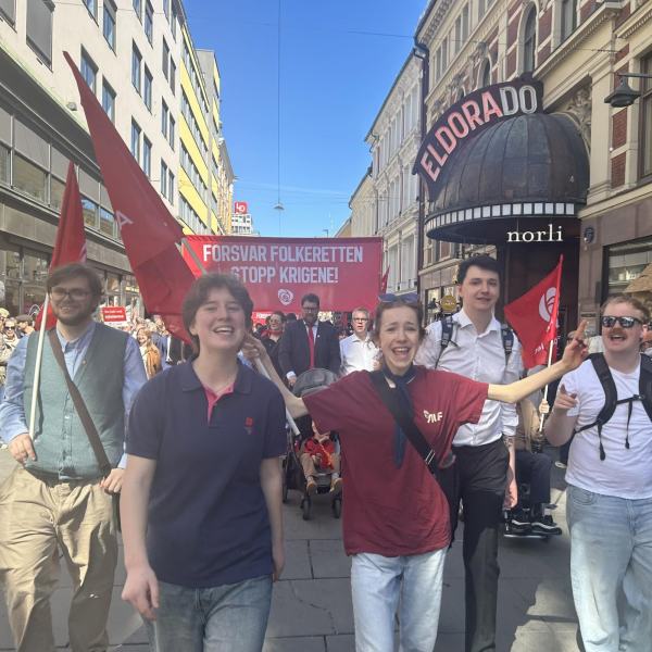 5 glade Astudere går foran en parole i 1. mai toget i Oslo med påskriften Forsvar folkeretten - stopp krigene. Bildet er fra en sidegate til Youngstorget.