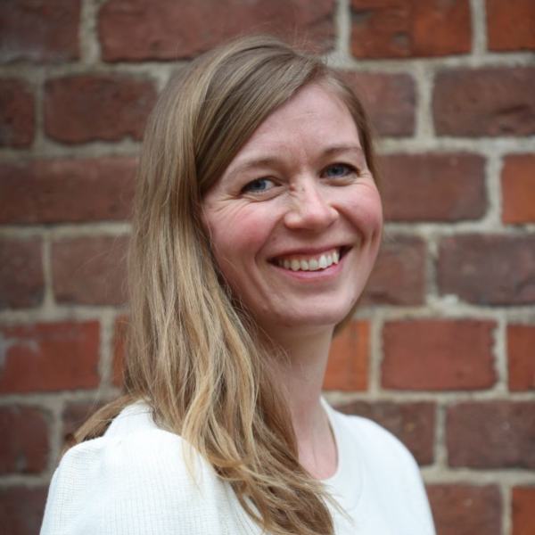 portrettbilde av kvinne i hvit bluse, med lang hår, som smiler til kamera. 