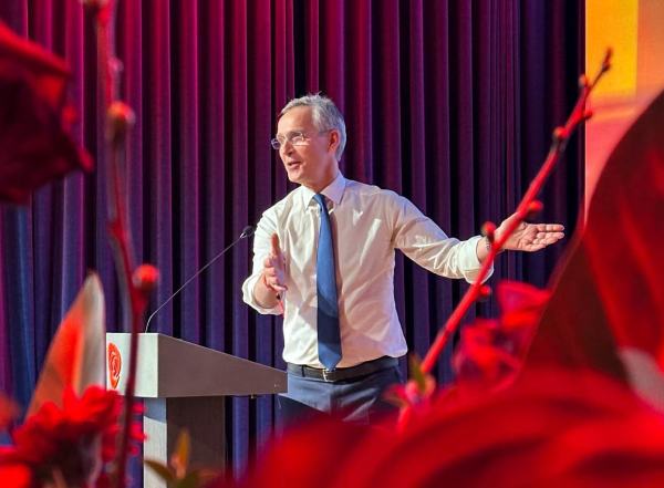 Finansminister Jens Stoltenberg står på en scene og snakker i hvit skjorte, blå dressbukse og blått slips.