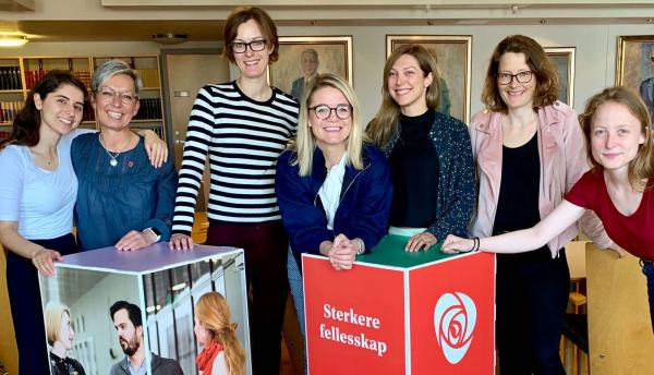 Styringsgruppa i kvinnenettverket står foran en boks med bilder av forskjellige mennesker, og en rød boks med partirosen og teksten "Sterkere fellesskap".