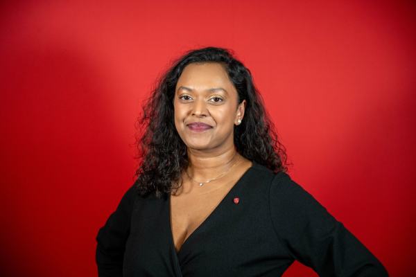 Kamzy Gunaratnam i sort kjole foran en rød vegg