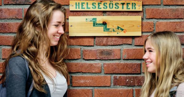Skoleelver som står ved helsesøster skilt