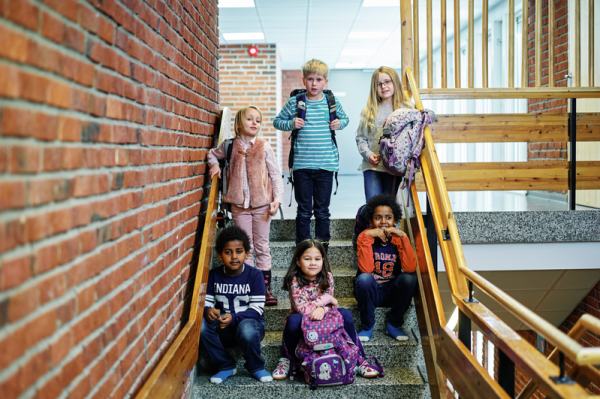 6 barn står i en trapp på en skole. Tre av barna sitter og tre av dem står på trappetrinnene over