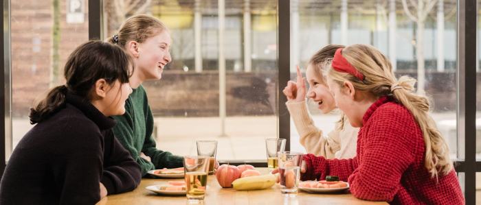 4 glade skolebarn som sitter rundt et bord og spiser skolemat sammen.