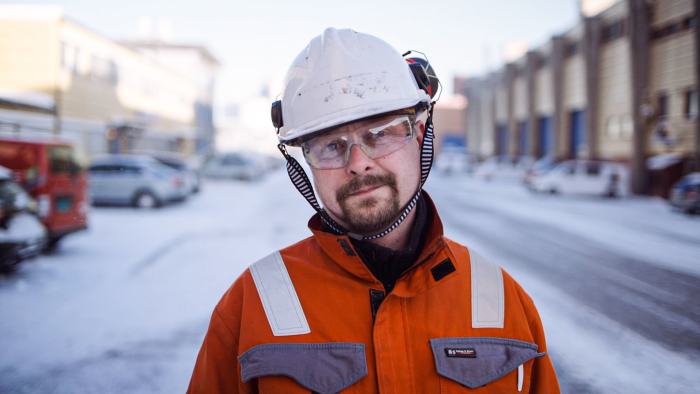 Mann med hjelm og orange kjeledress. Utendørs.