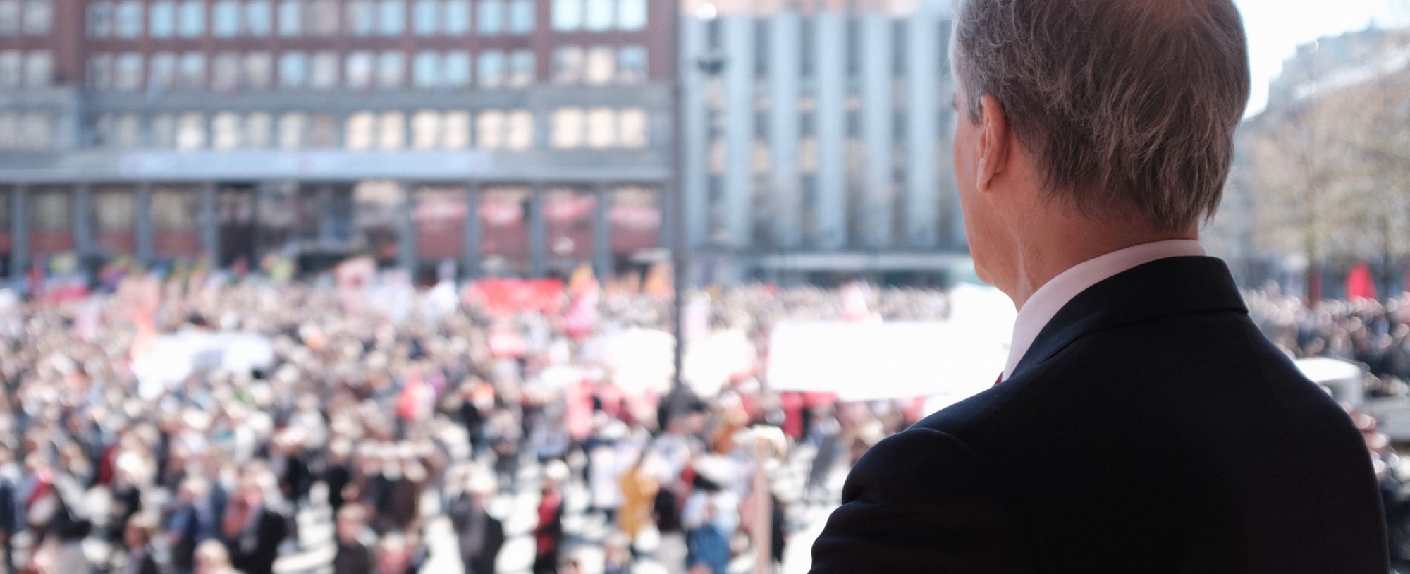 Jonas Gahr Støre bakfra med utsikt over Youngstorget mens han holder 1. mai-tale. Mange mennesker står nede på torget.