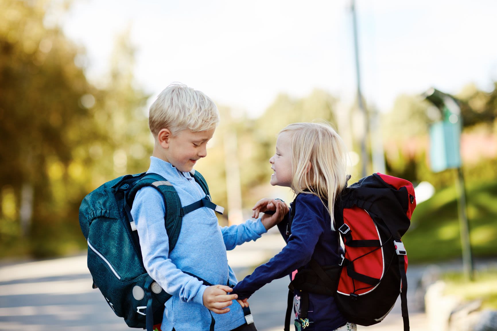 Liten gutt og liten jente med skolesekker stående smilende mot hverandre