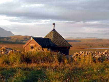 A beautiful 10m² camping cabin situated atop a grassy hill overlooking a valley with mountains in the background.