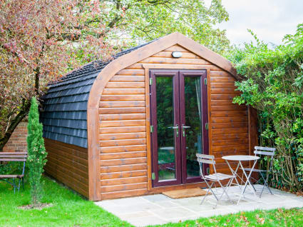 A camper sitting beside a hedge with a table and chairs at it's front.