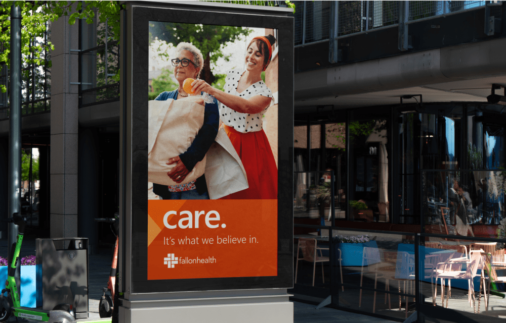 Outdoor advertisement featuring two people smiling and carrying laundry, with the text "care. It's what we believe in." and a logo for #allonhealth.