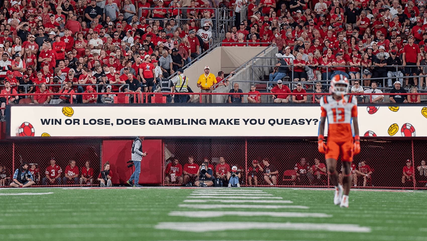 A football player stands on the field in front of a crowd and a stadium sign that reads, "WIN OR LOSE, DOES GAMBLING MAKE YOU QUEASY?.