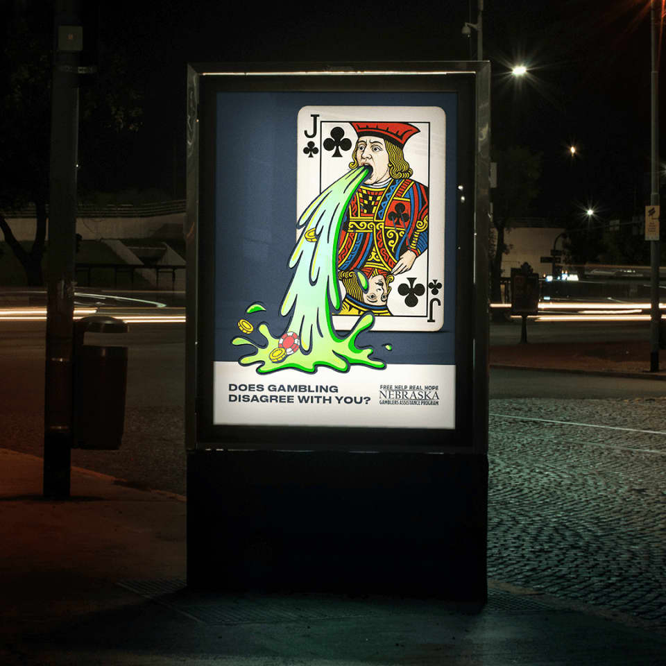 A bus stop ad at night shows a cartoon Jack of Clubs vomiting chips and dice, with the text, "DOES GAMBLING DISAGREE WITH YOU?" and a Nebraska problem gambling helpline.