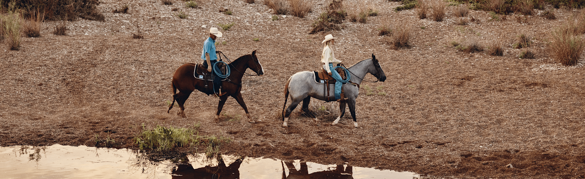 Woman and a man on horse back riding near water.