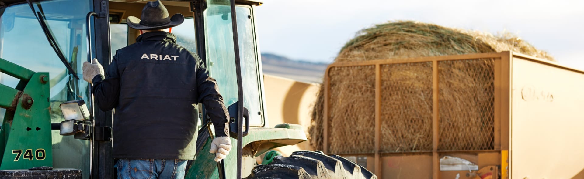 man wearing Ariat softshell jacket getting into a tractor