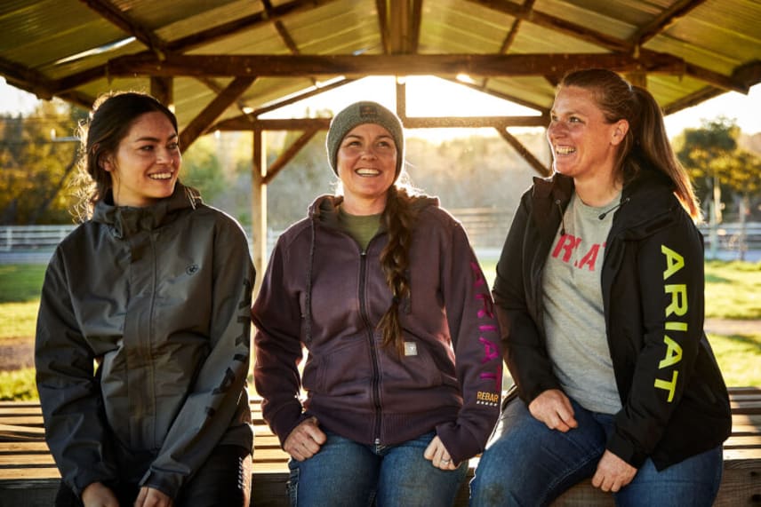 three women wearing ariat sitting in a ranch