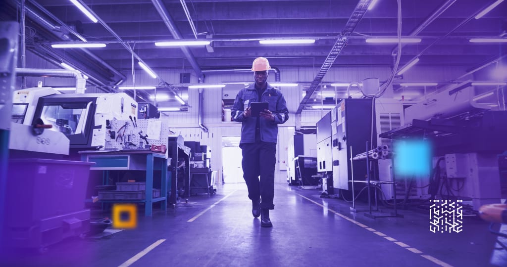 African American Male Worker in a Yellow Hard Hat Walks Through a Modern Factory, Inspecting Equipment and Recording Data on a Tablet Computer