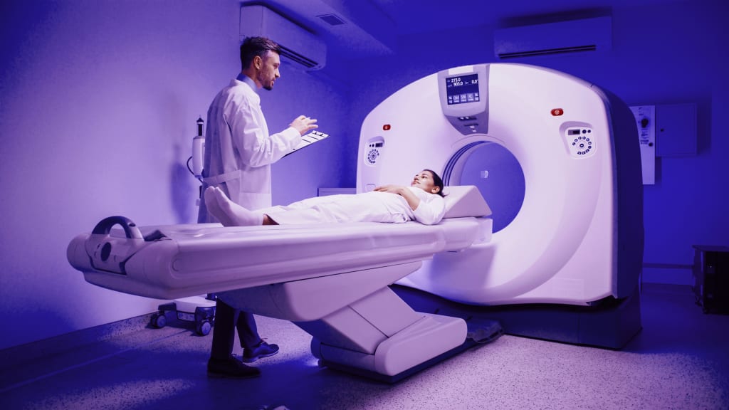 Male physician gesturing at female patient resting on scan bed. Woman relaxes before CT procedure begins inside brightly lit medical imaging room.