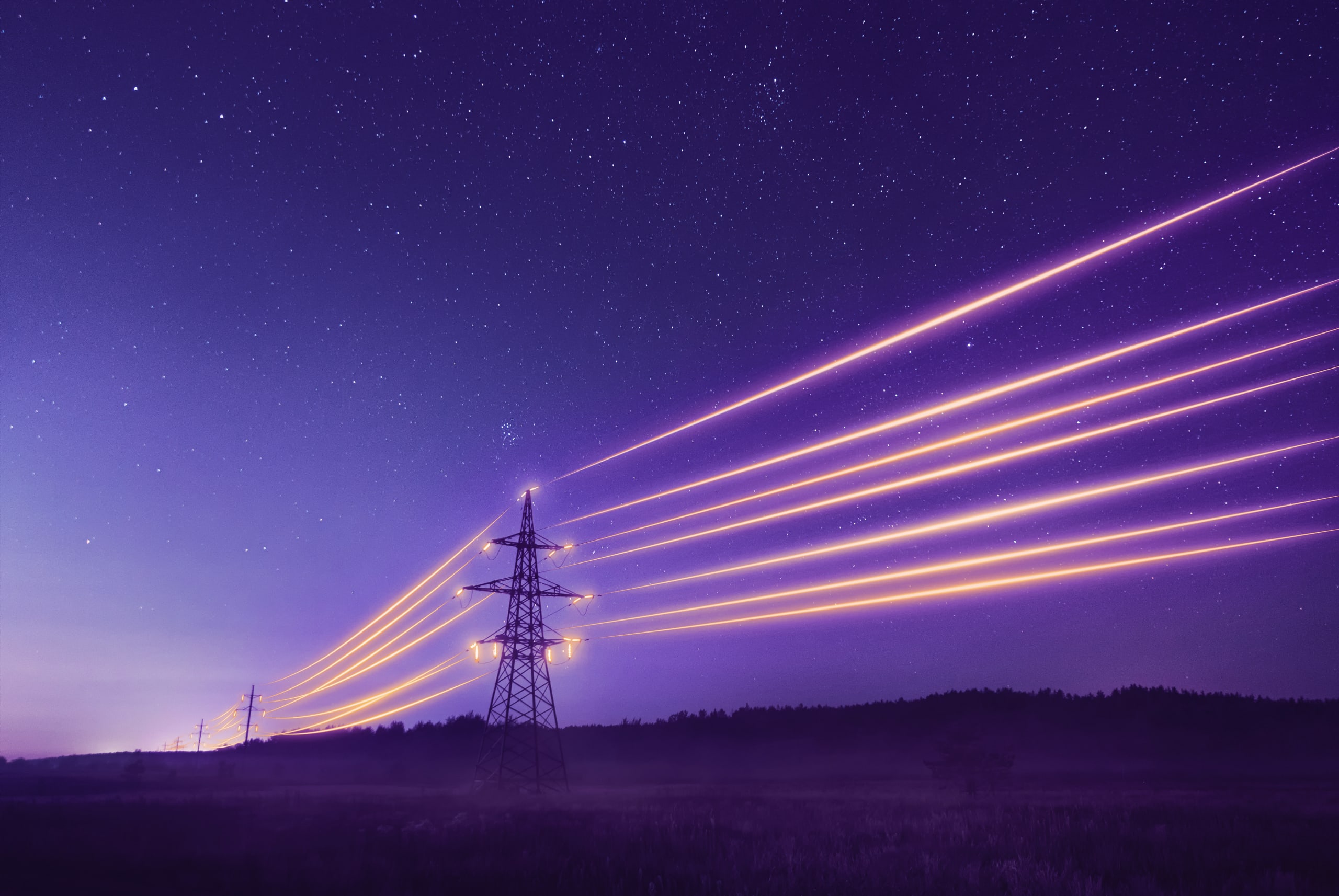 Electricity transmission towers with glowing wires at night
