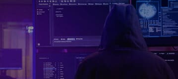 back of hacker in a hoodie sitting at a computer
