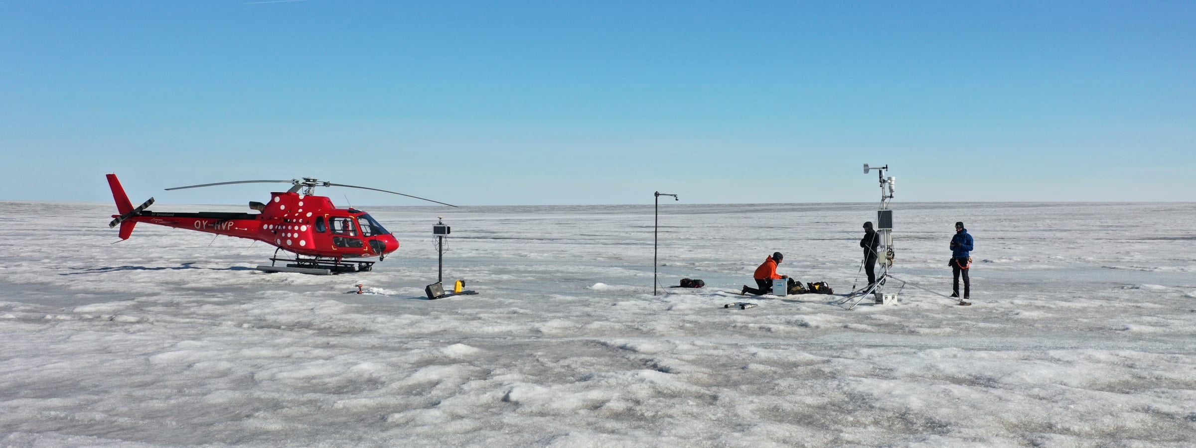 A helicopter and field team working beside monitoring equipment on the Greenland ice sheet