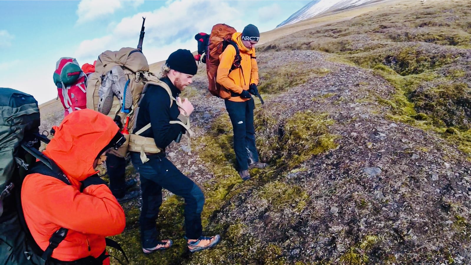 Svalbard expedition team moving over rocky tundra with full packs