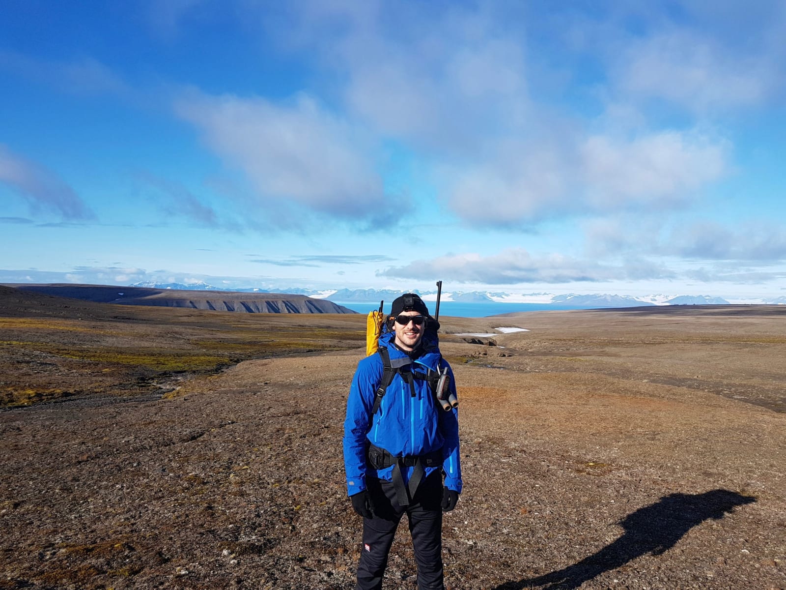 Svalbard expedition member with pack in open terrain above a fjord