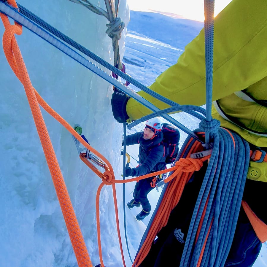 Ice climber moving on a roped ice wall with climbing equipment in the foreground