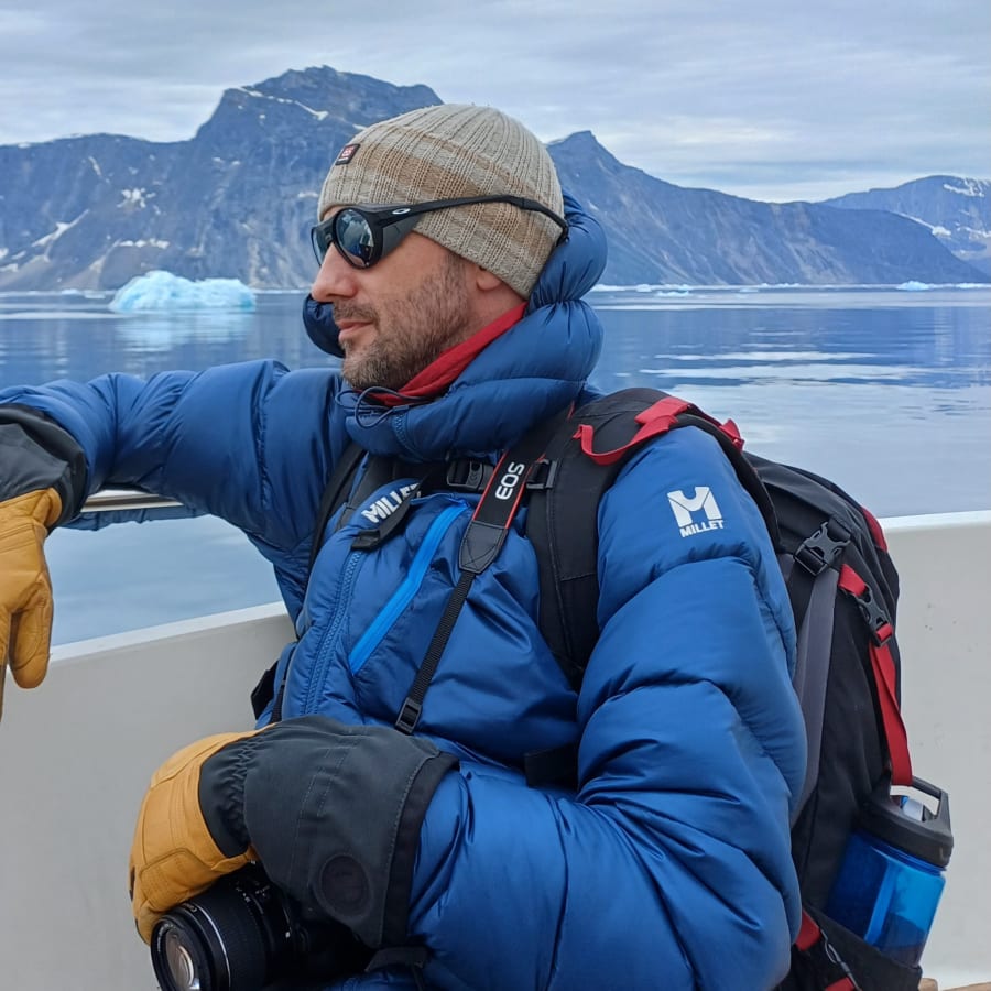 Arnar Ingi on a boat in Greenland with icebergs and mountains behind him