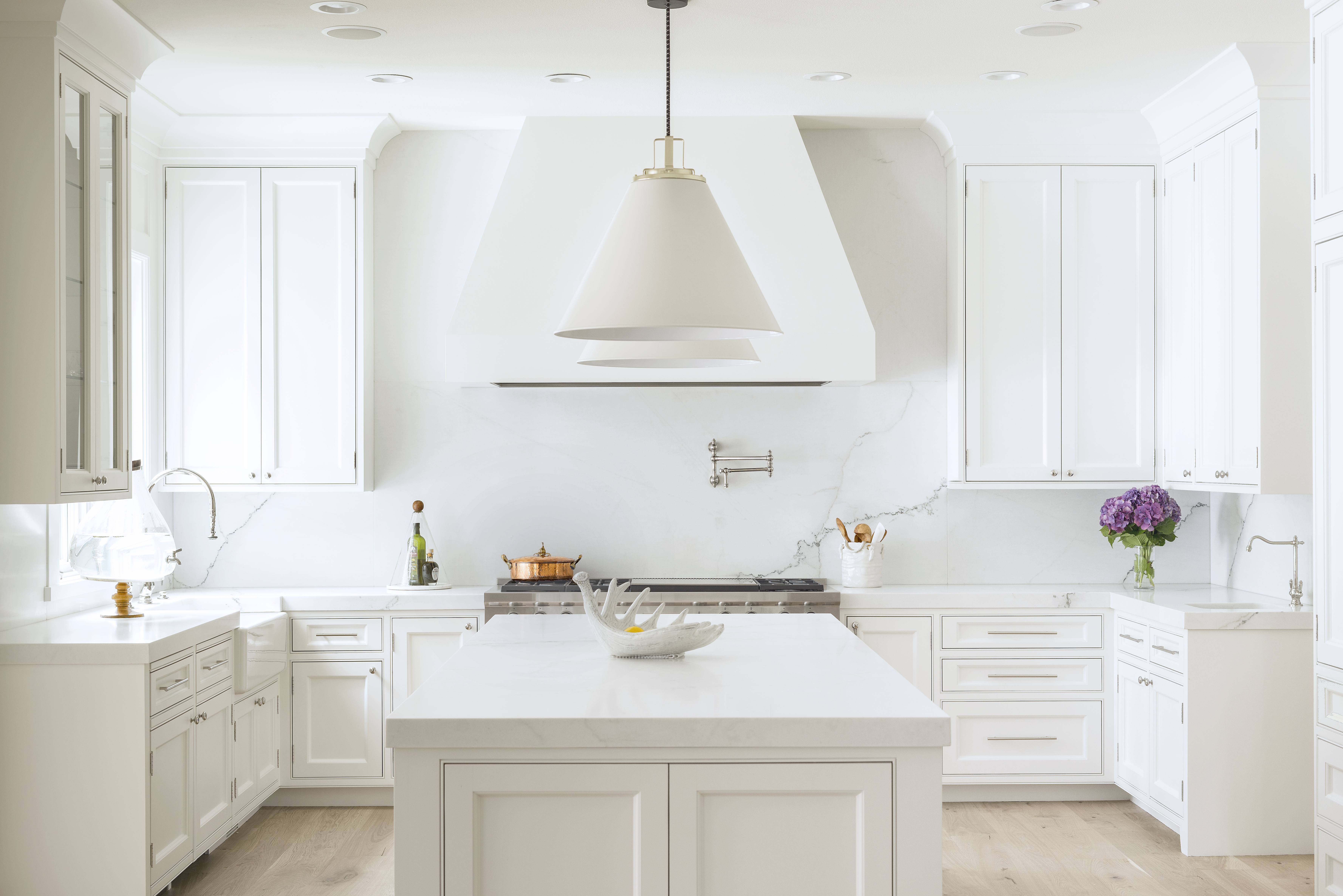 Bright white kitchen with quartz island, custom cabinetry, and statement range hood