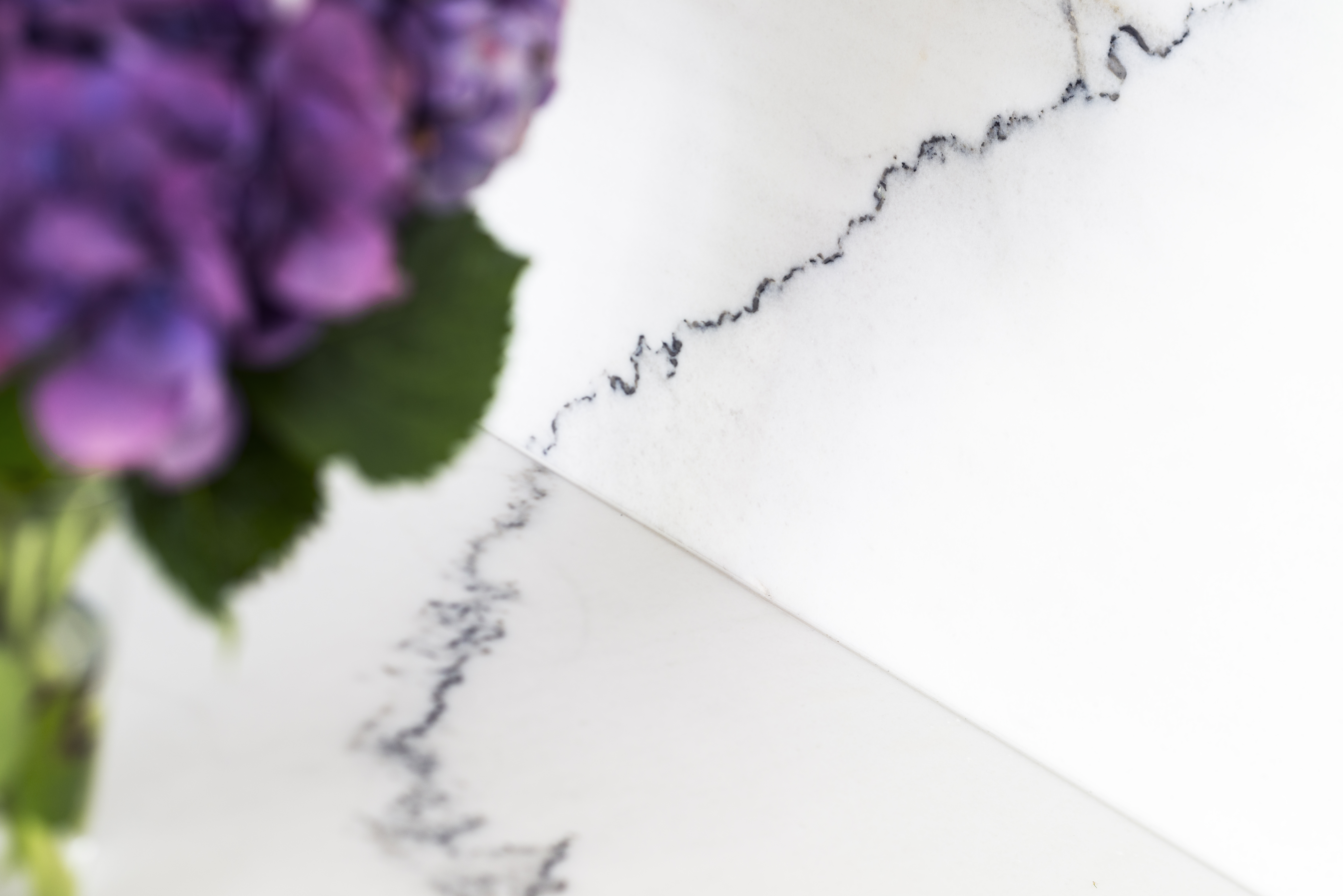White quartz backsplash with subtle veining and decorative purple hydrangea arrangement