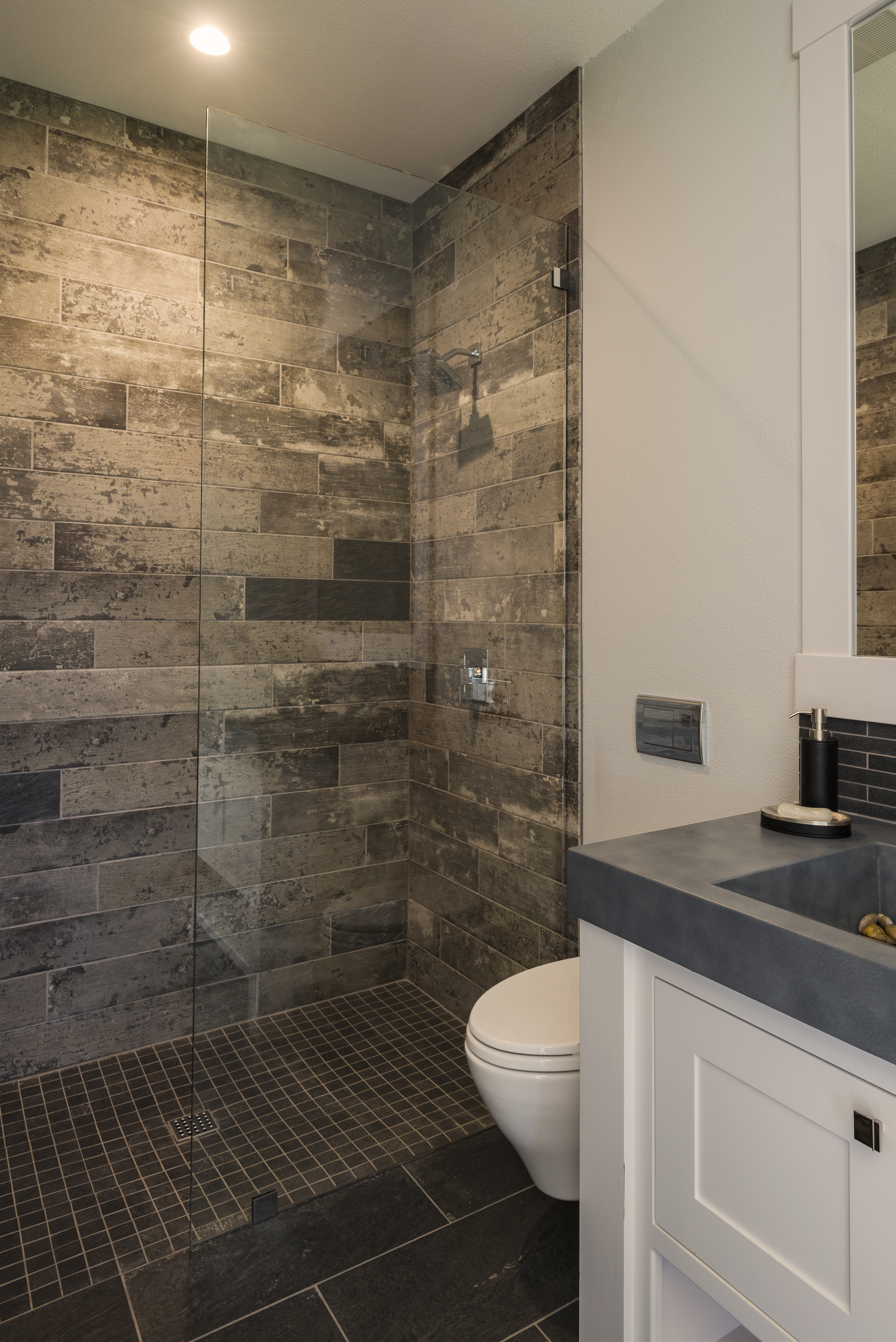 Modern bathroom with glass shower enclosure, dark tile walls, and floating vanity