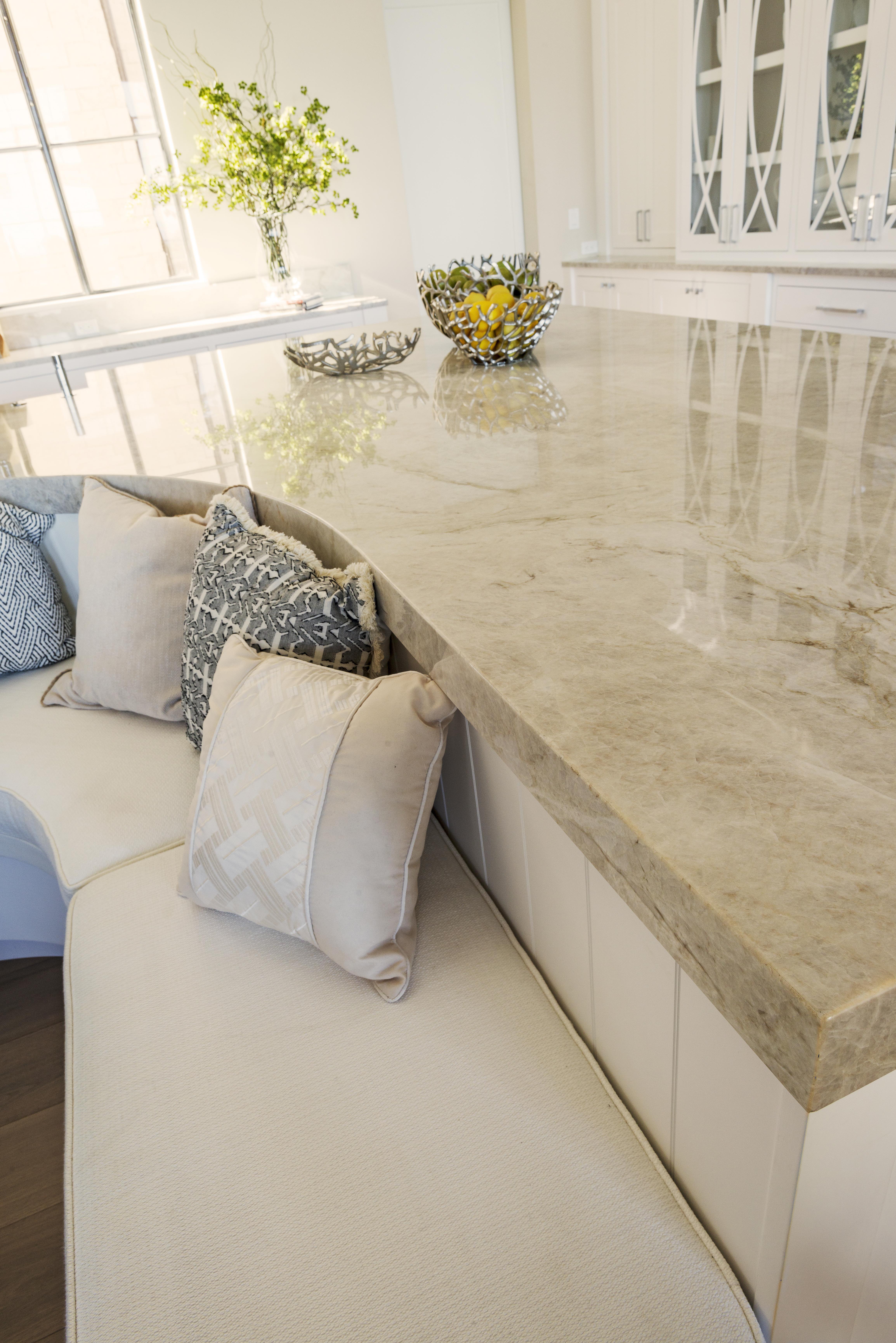Polished stone kitchen countertop with decorative bowls and cushioned seating underneath