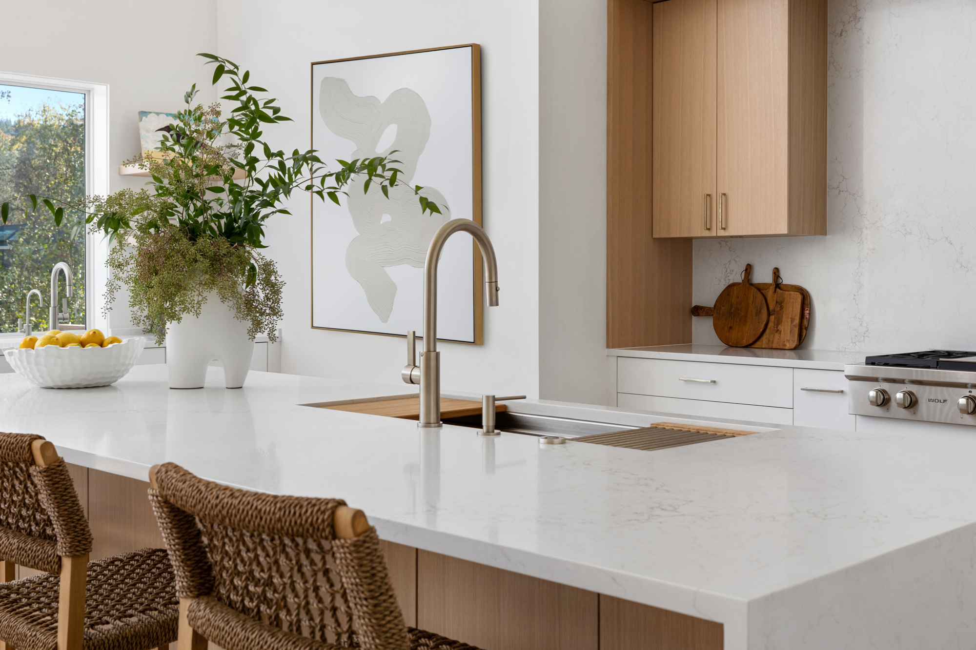 Modern white kitchen island with integrated sink, wood cabinetry, and woven bar stools
