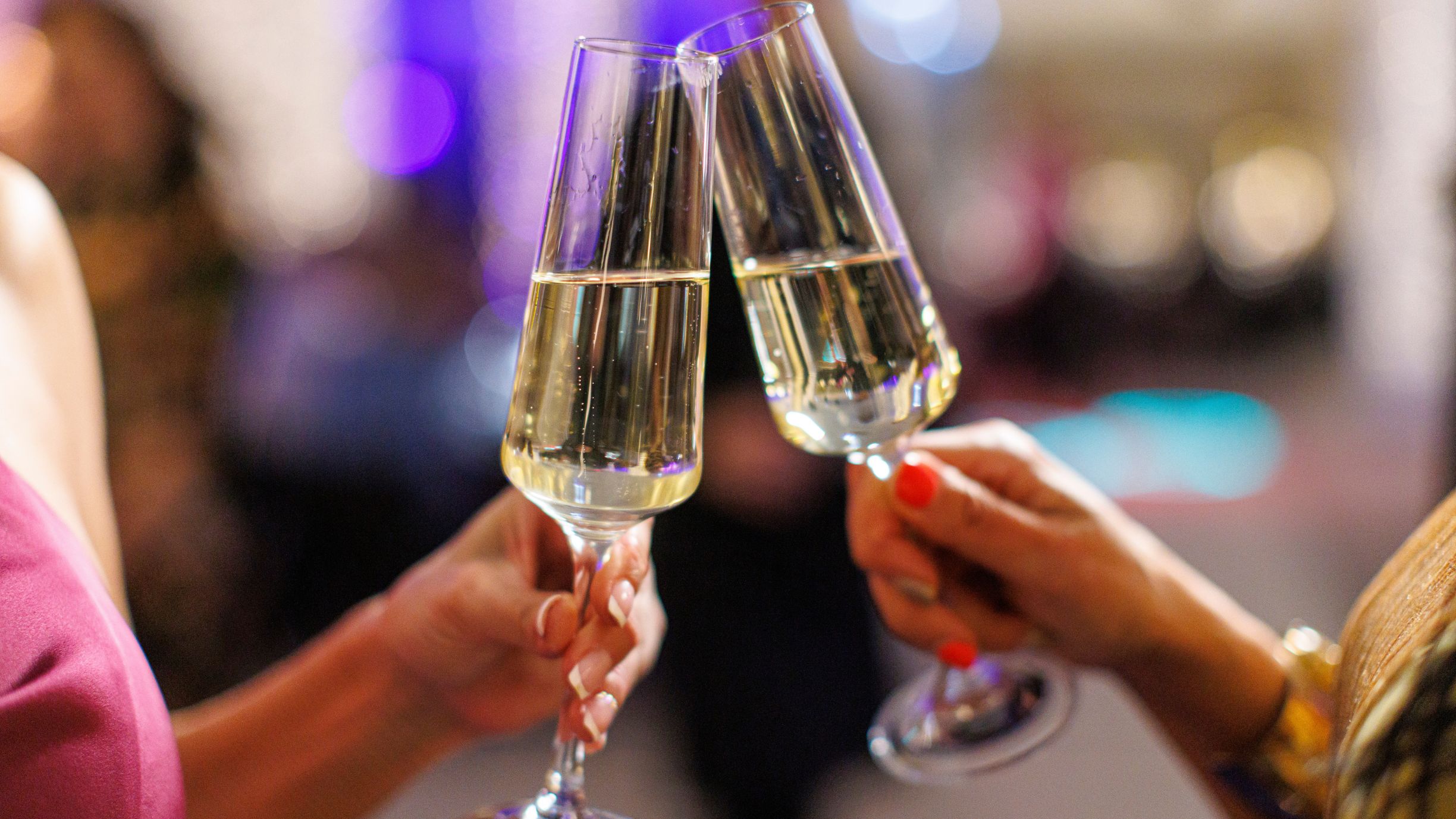 Feminine hands holding the glasses by the stem; in focus—nails with classic French manicure and bright orange polish.