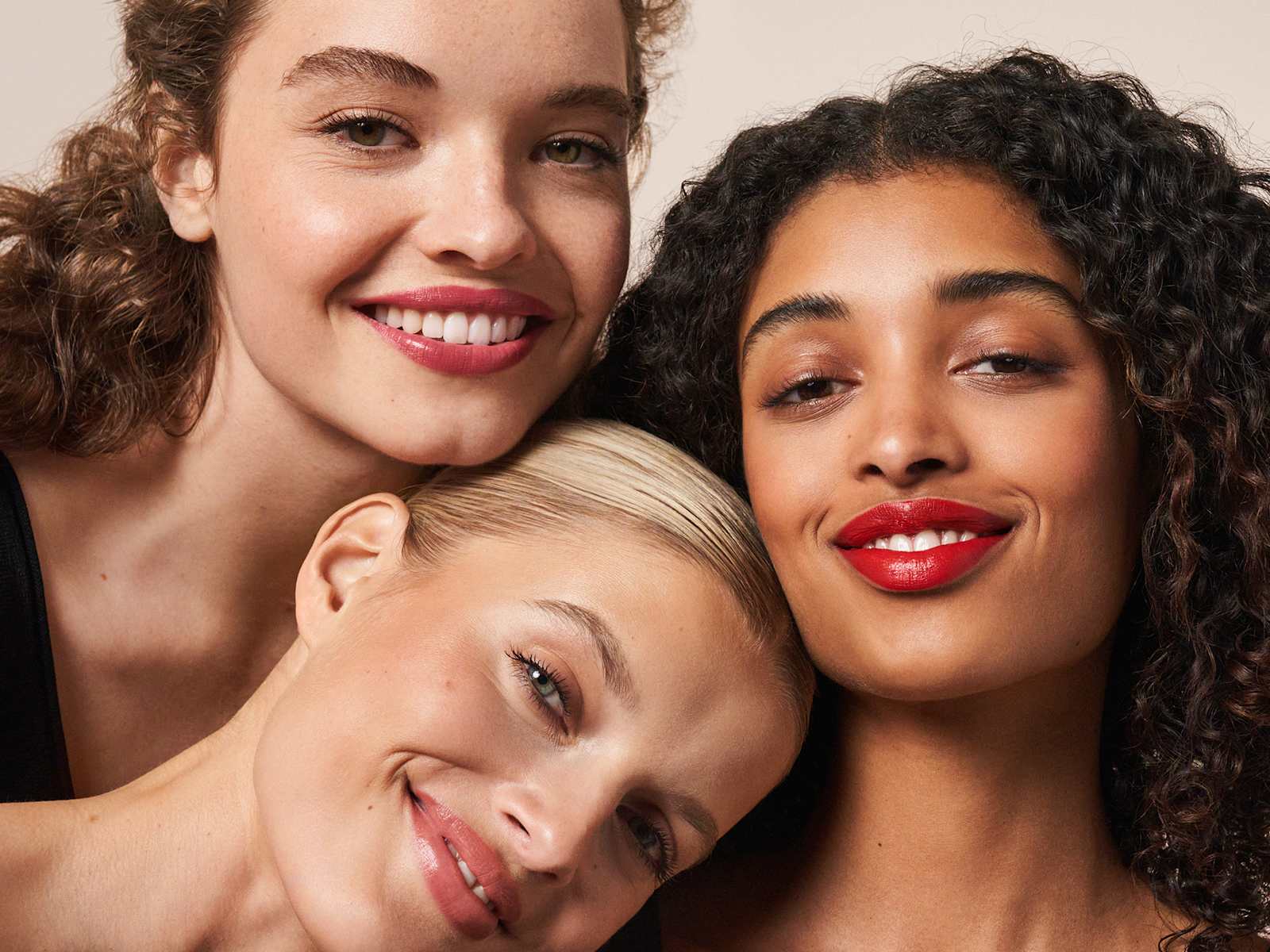 Trois modèles aux teints différents avec rouge à lèvres rouge, posant côte à côte en souriant.