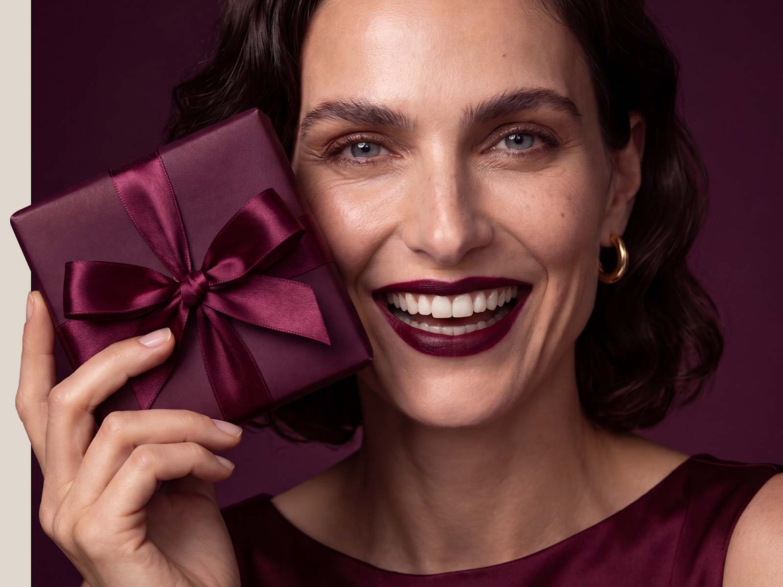 Beauty-Porträt einer lächelnden Frau mit dunklem Lippenstift und bordeauxroter Geschenkbox