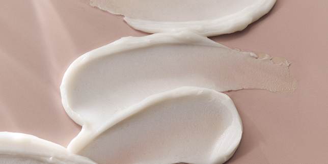 Texturaufnahme einer weißen Creme mit geschmeidiger Oberfläche auf rosigem Hintergrund