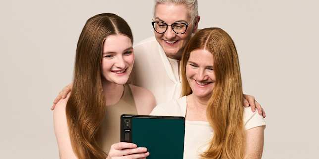 Gruppenporträt von drei lächelnden Frauen beim gemeinsamen Blick auf ein Tablet
