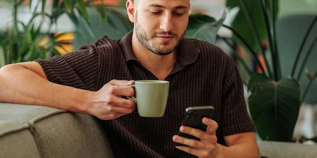 Porträt eines Mannes mit Kaffeetasse und Smartphone auf einem Sofa
