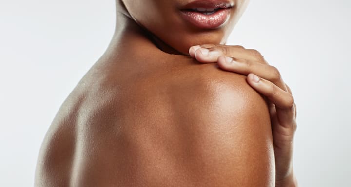 Femme touchant son épaule avec la main, gros plan d’une peau soignée et lumineuse